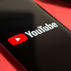 An image of a black phone on a flat surface with the red and white YouTube logo is shown.